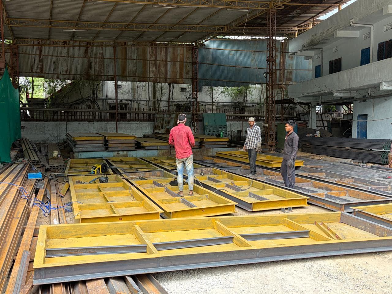 Steel framework fabrication — workers assembling structural steel at Jeedimetla factory, Hyderabad